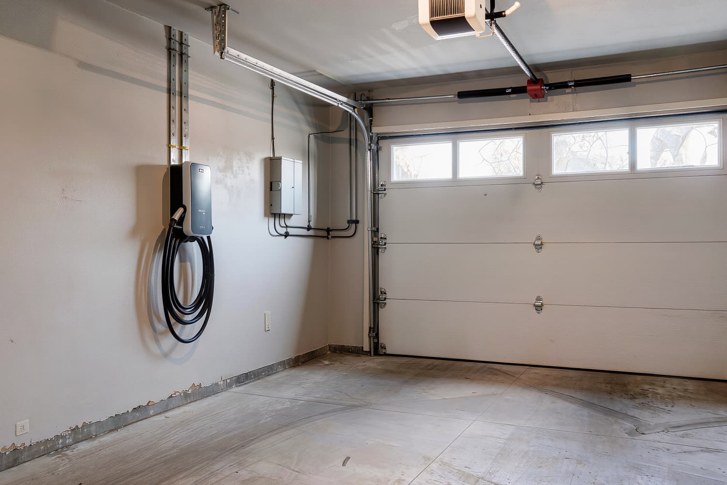 Wall-mounted electric vehicle charger installed level beside a small subpanel in a home garage