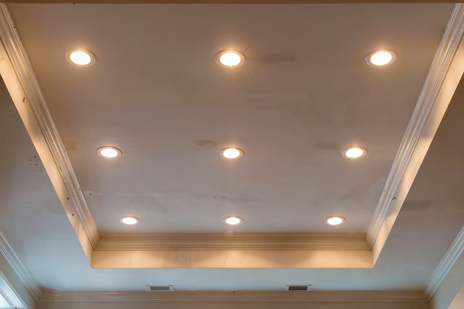 Looking up at eight recessed downlights set flush in an even grid across a flat white ceiling