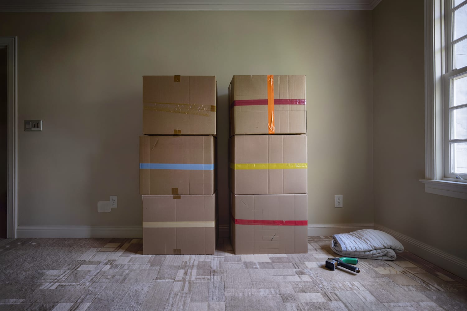 Plain kraft moving cartons stacked in even tiers and sorted by coloured tape bands in a bare room