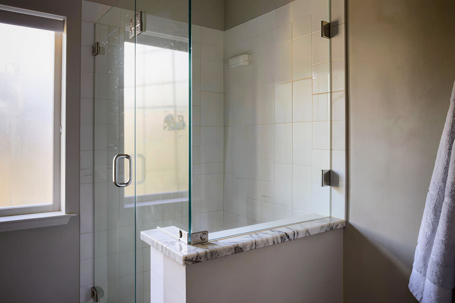Detail of a frameless glass shower screen dried spot free beside a marble threshold and folded towel