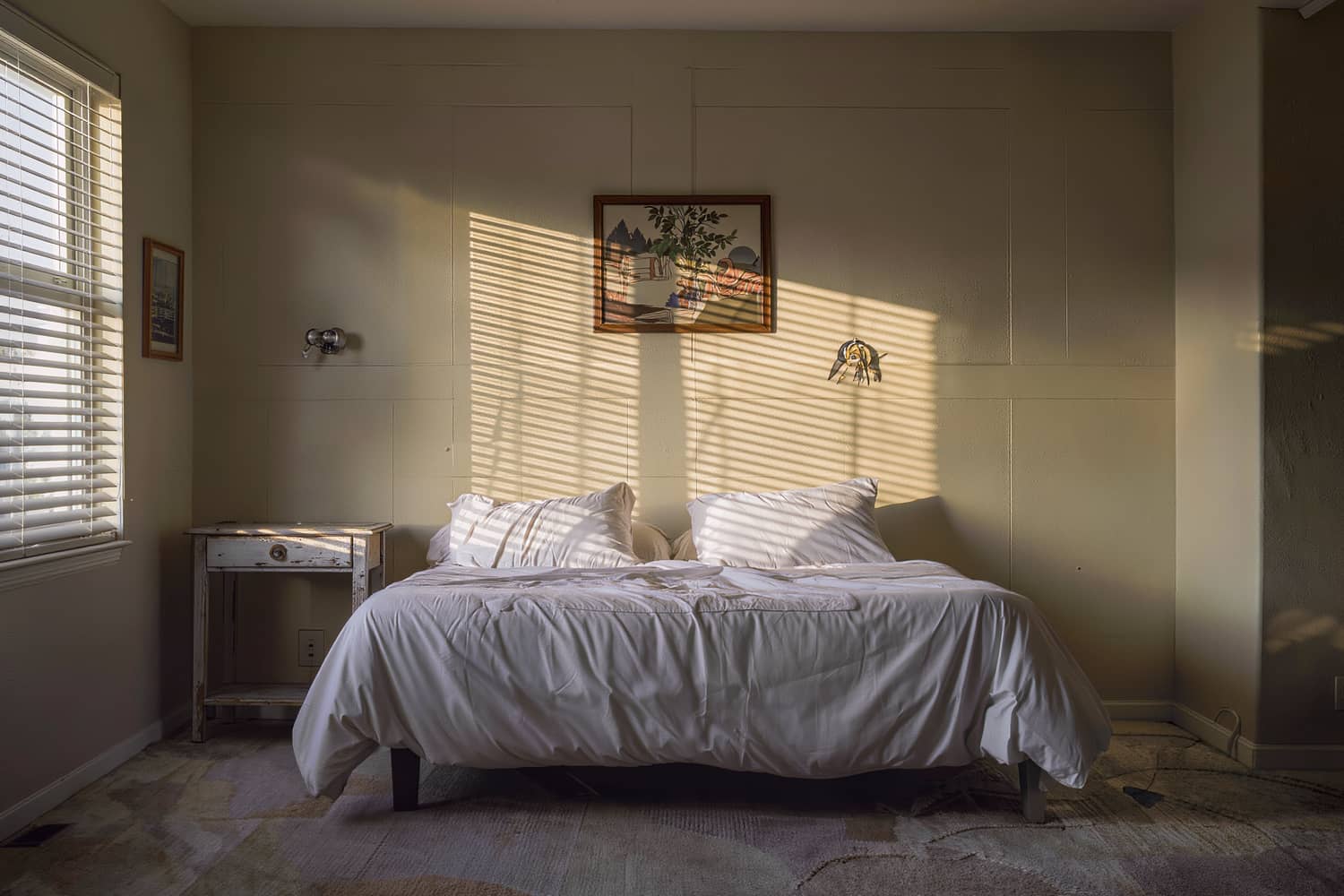 Made bed with crisp white bedding under slatted blind shadows in late afternoon