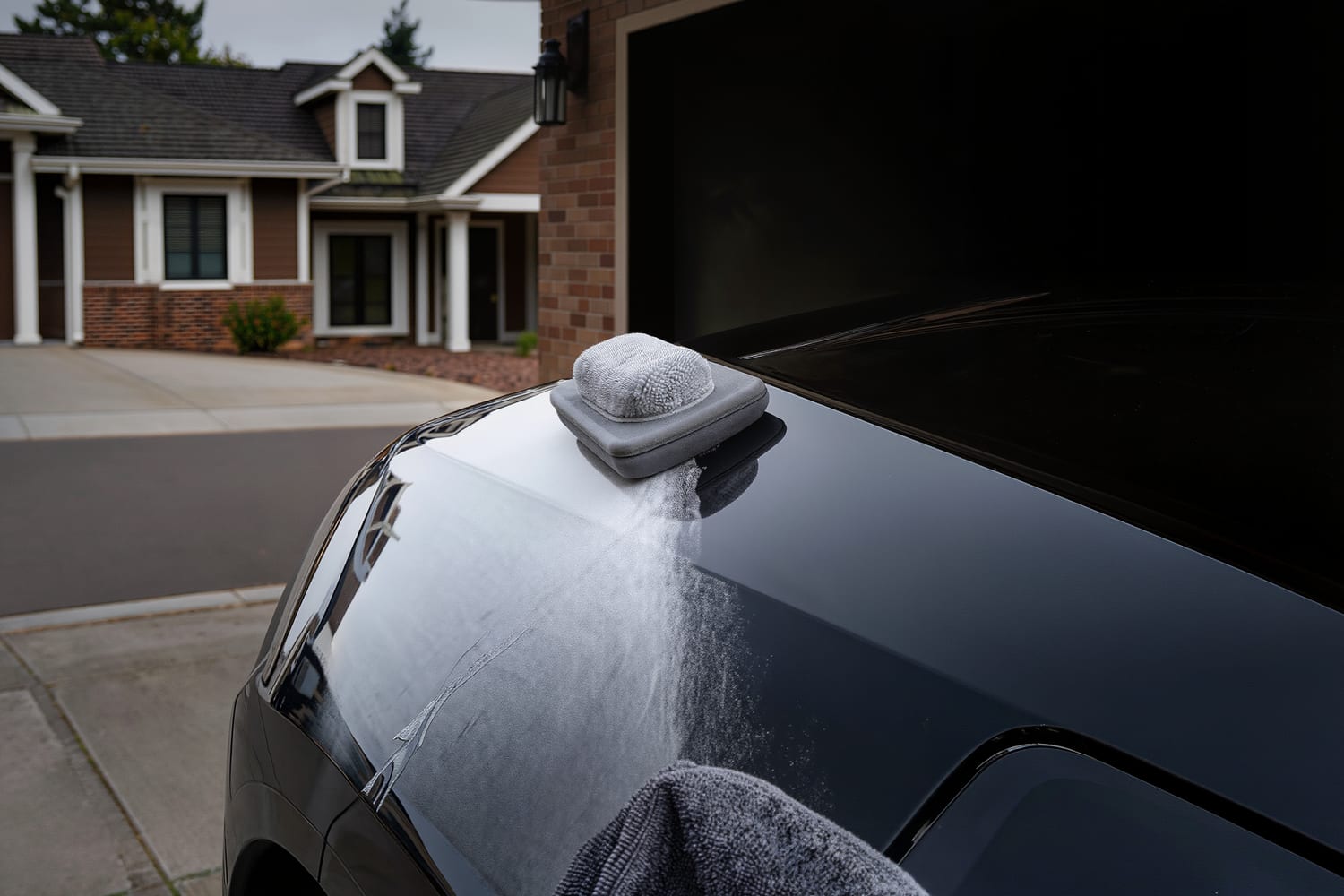Foam applicator pad on a dark hood beside a half buffed band of wax haze