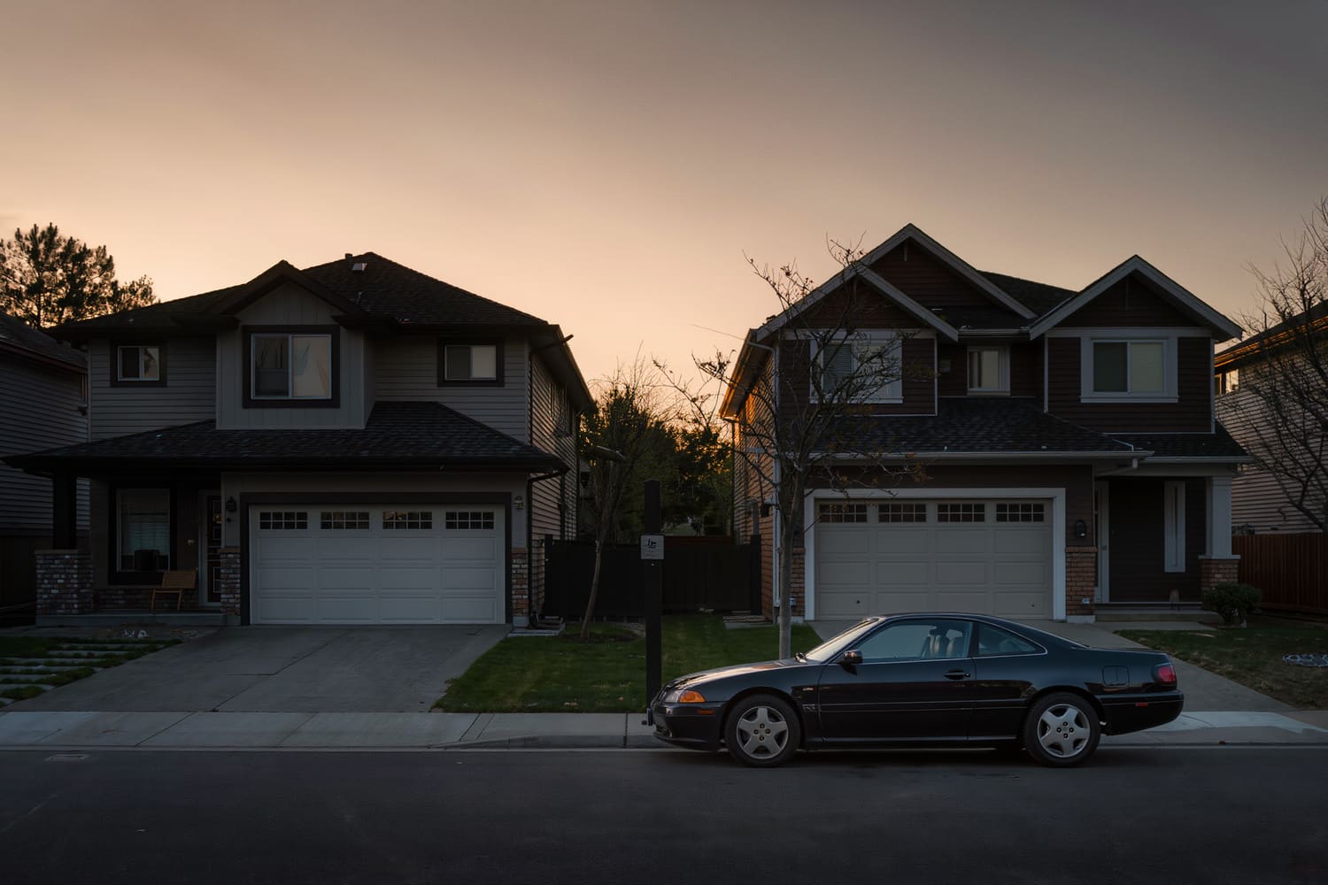 Rear of a dark coupe small in frame on a residential street at dusk
