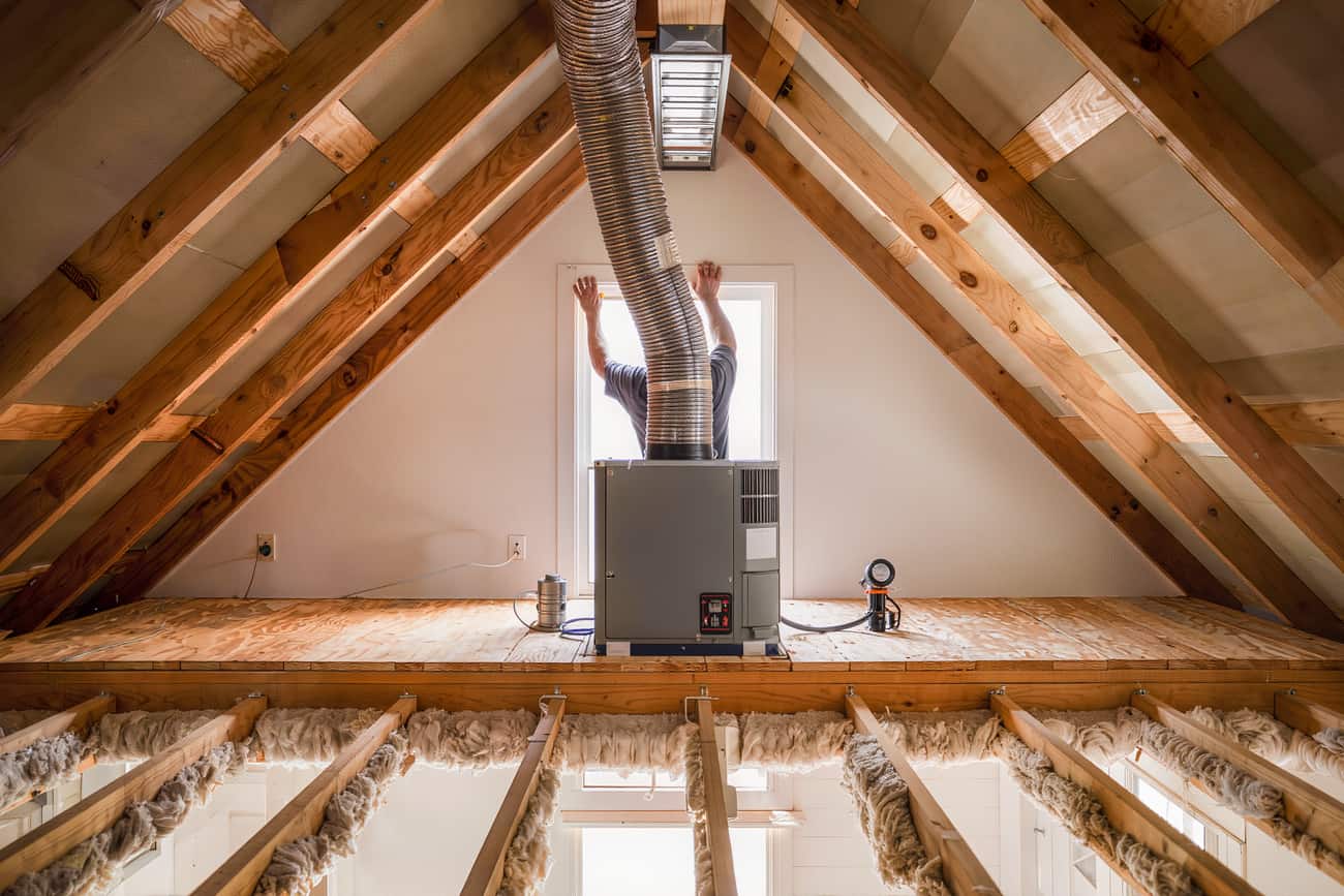 Attic air handler on a plywood platform being inspected, flex duct running to the plenum