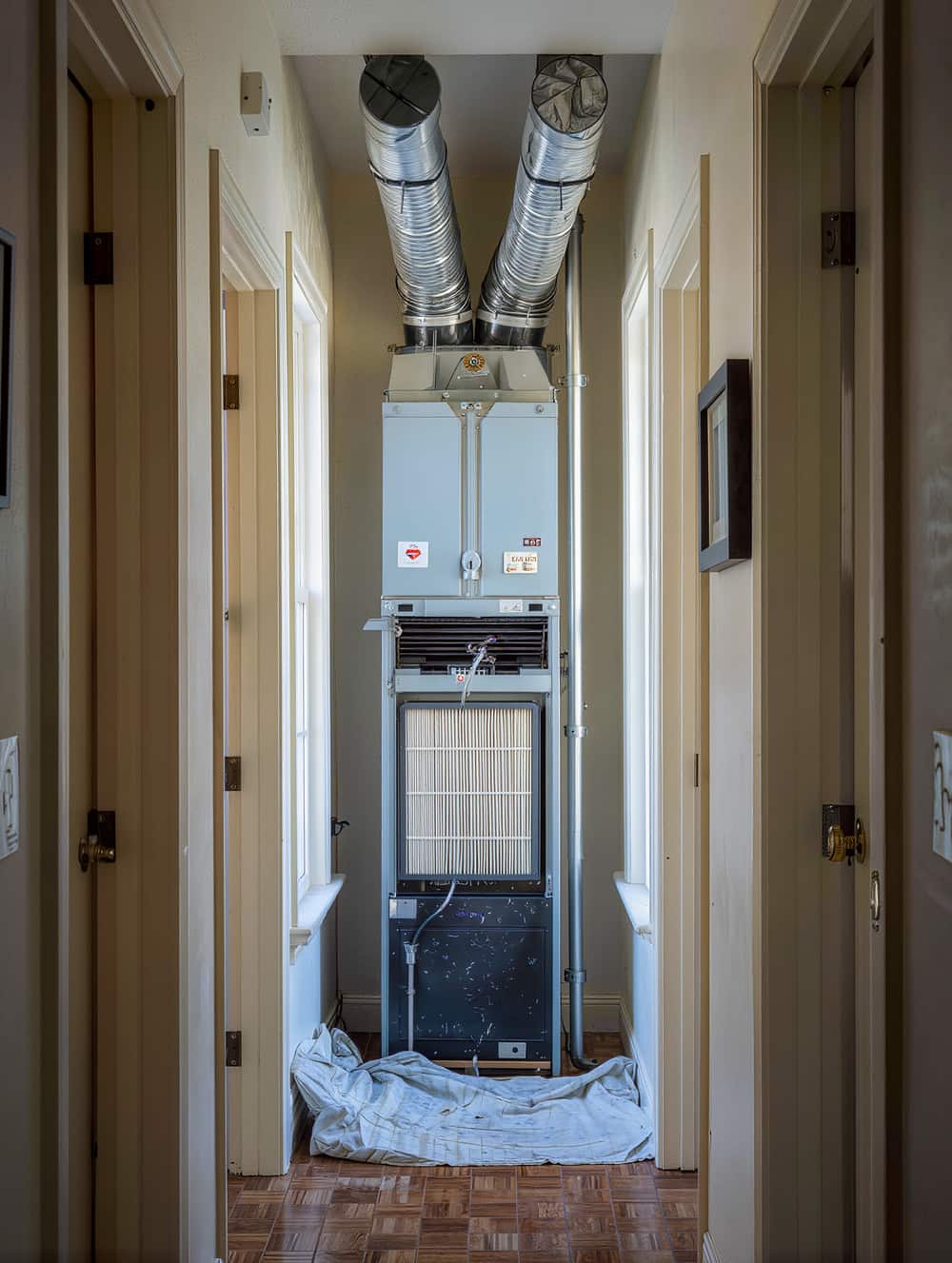 Vertical indoor air handler in a hallway closet with a clean pleated filter half slid into the rack