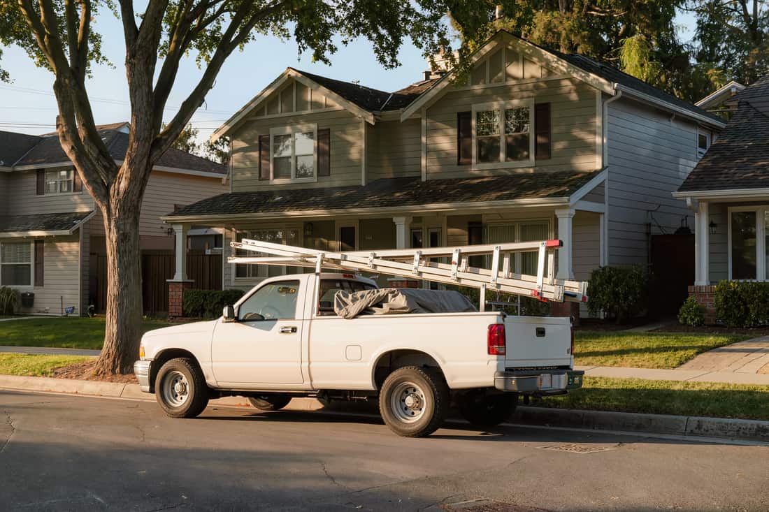 Trade pickup with a utility bed and ladder rack parked at the curb on a residential street
