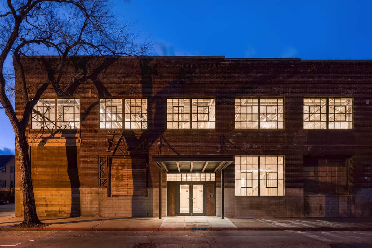 A converted warehouse exterior at twilight with new glazing lit from within.
