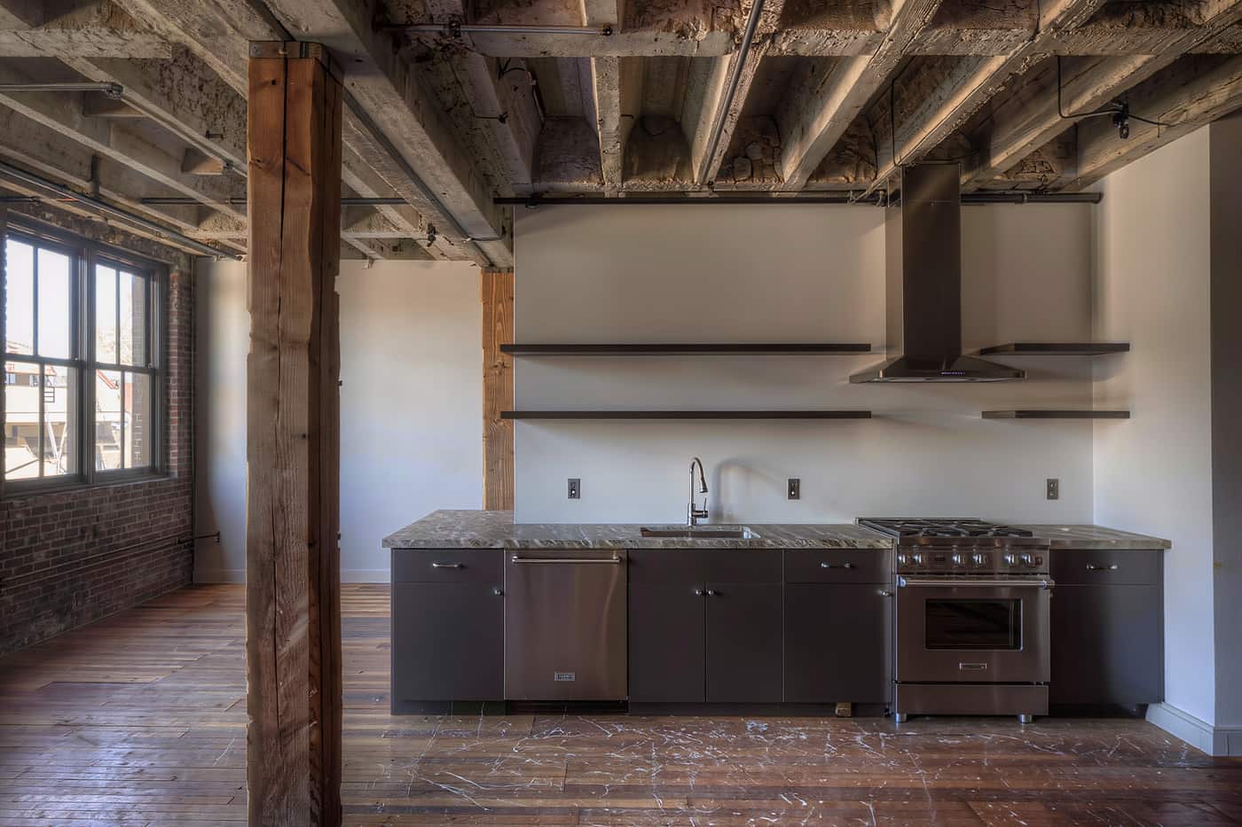 A loft apartment kitchen after conversion with a concrete ceiling above new cabinetry.