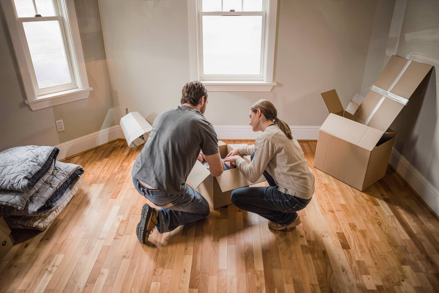 A couple unpacking in the front room of their new home, seen from behind.