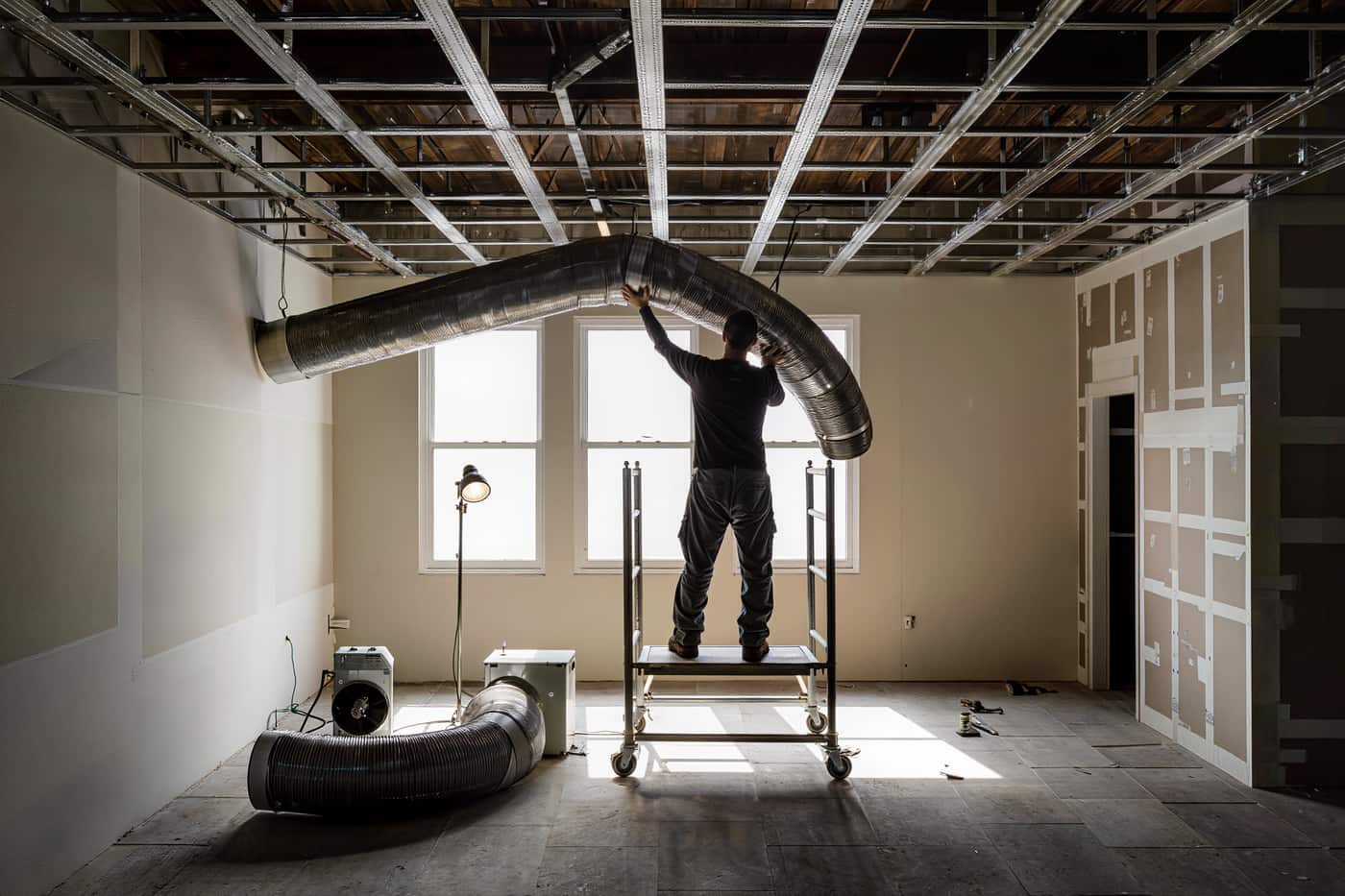 A worker on a rolling scaffold hanging spiral duct in an unfinished tenant space