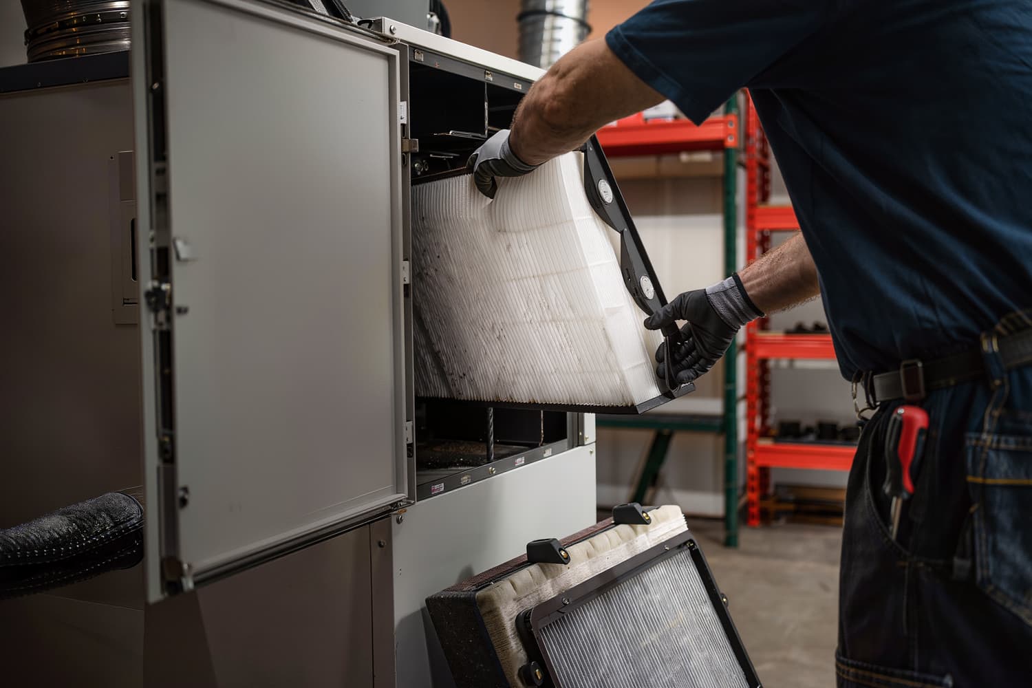 Gloved hands sliding a pleated filter into the rack of a commercial air handler