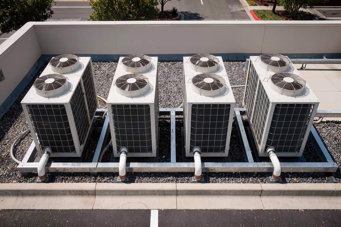 A row of air-cooled condensing units on equipment rails across a flat roof at midday