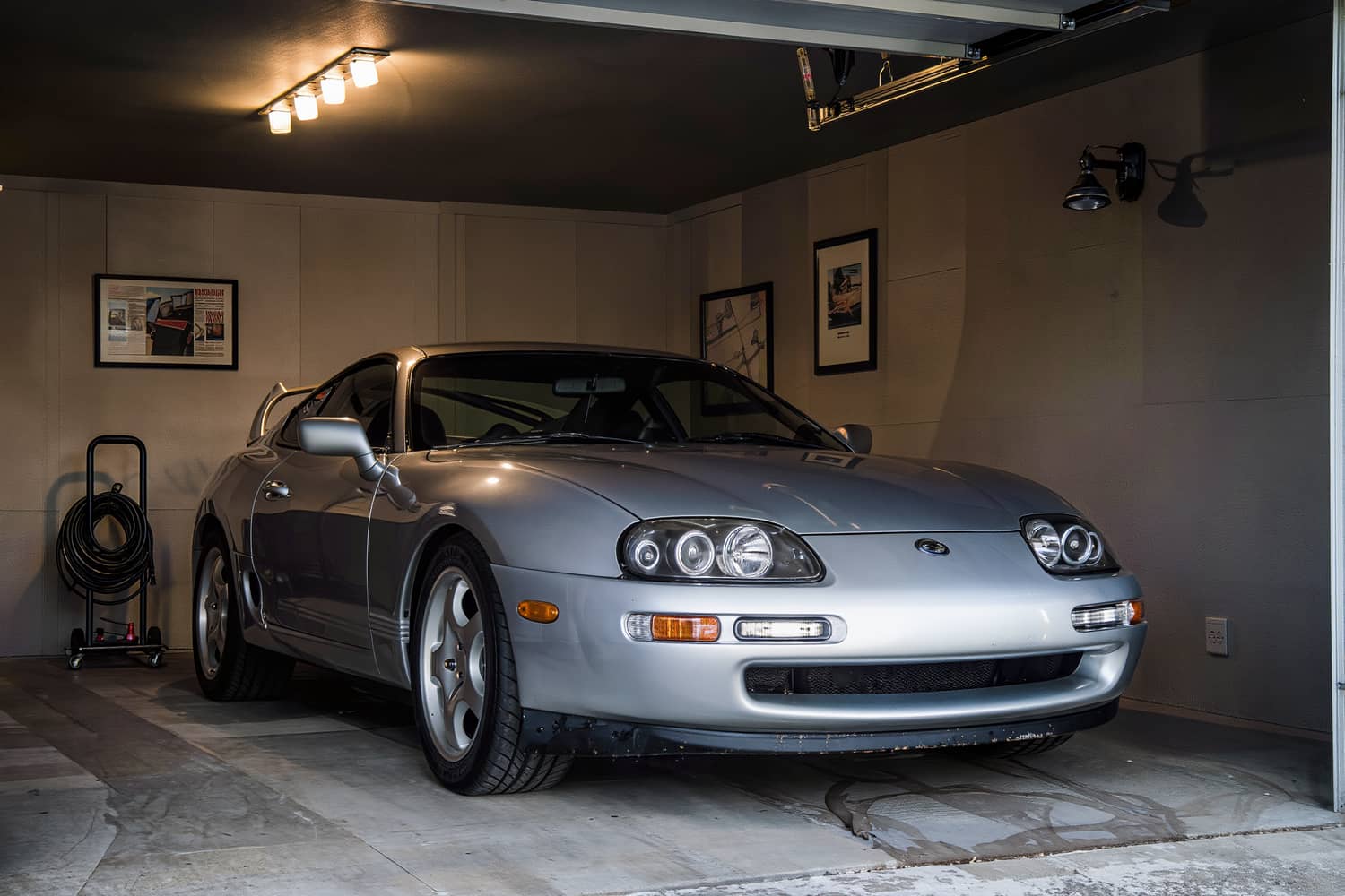 Silver coupe inside a closed home garage under a single overhead shop light