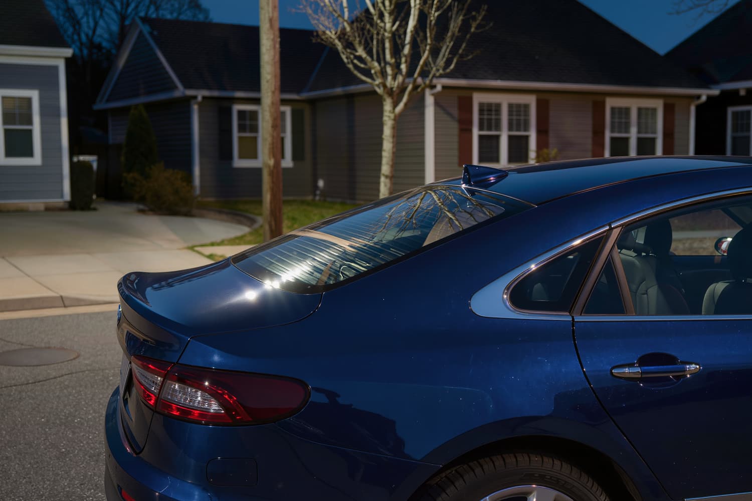 Rear quarter of a blue sedan at night reflecting a single street lamp