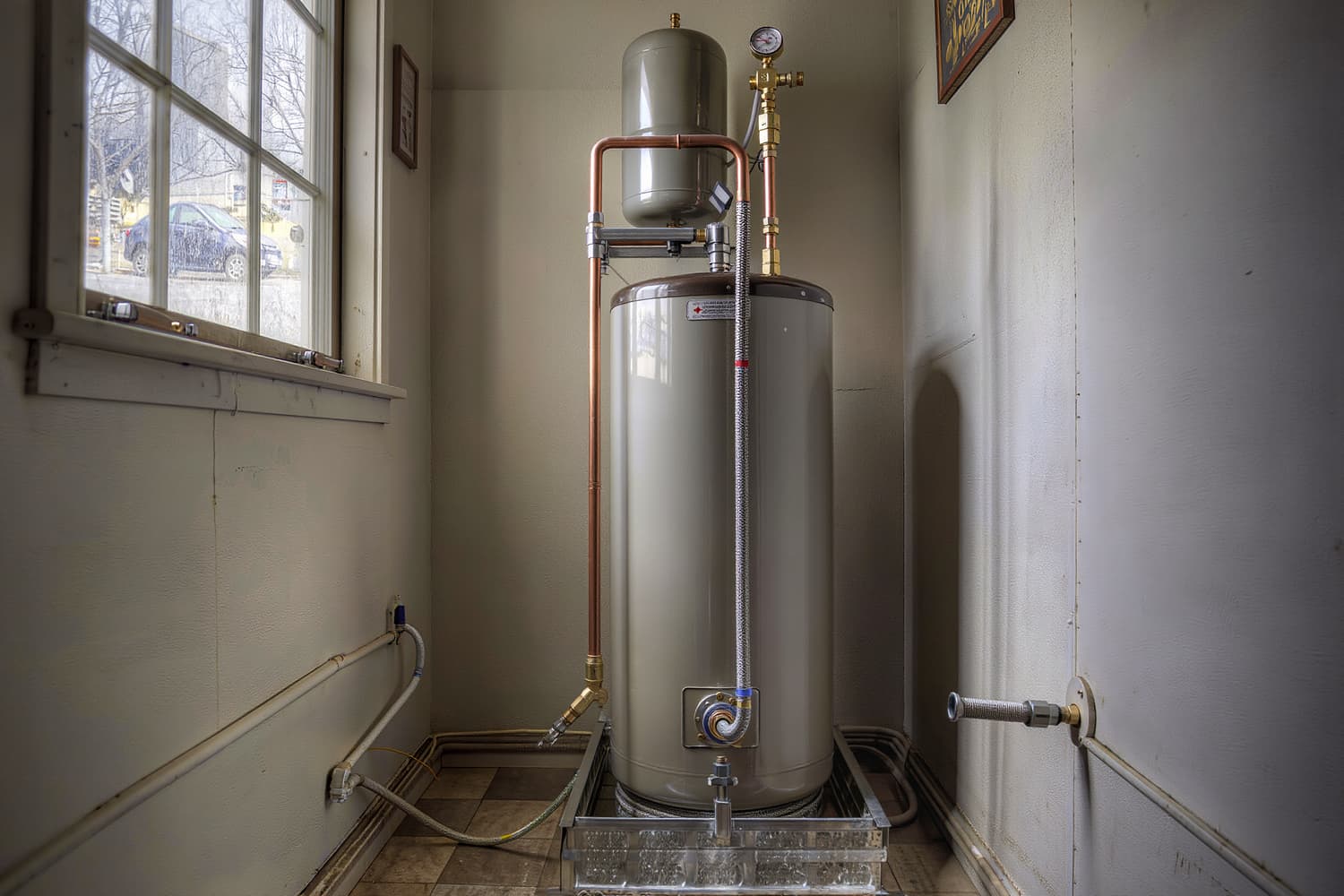 Newly installed tank water heater on a drain pan in a residential utility closet