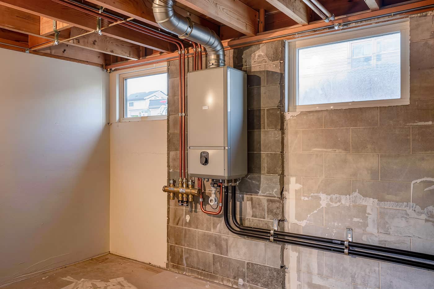 Wall-mounted tankless water heater with copper runs and isolation valves in an unfinished basement