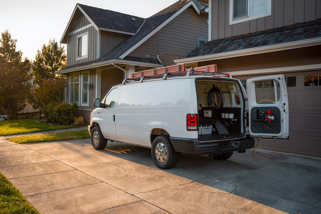 Plain white service van parked on a driveway with its rear doors open on plumbing stock