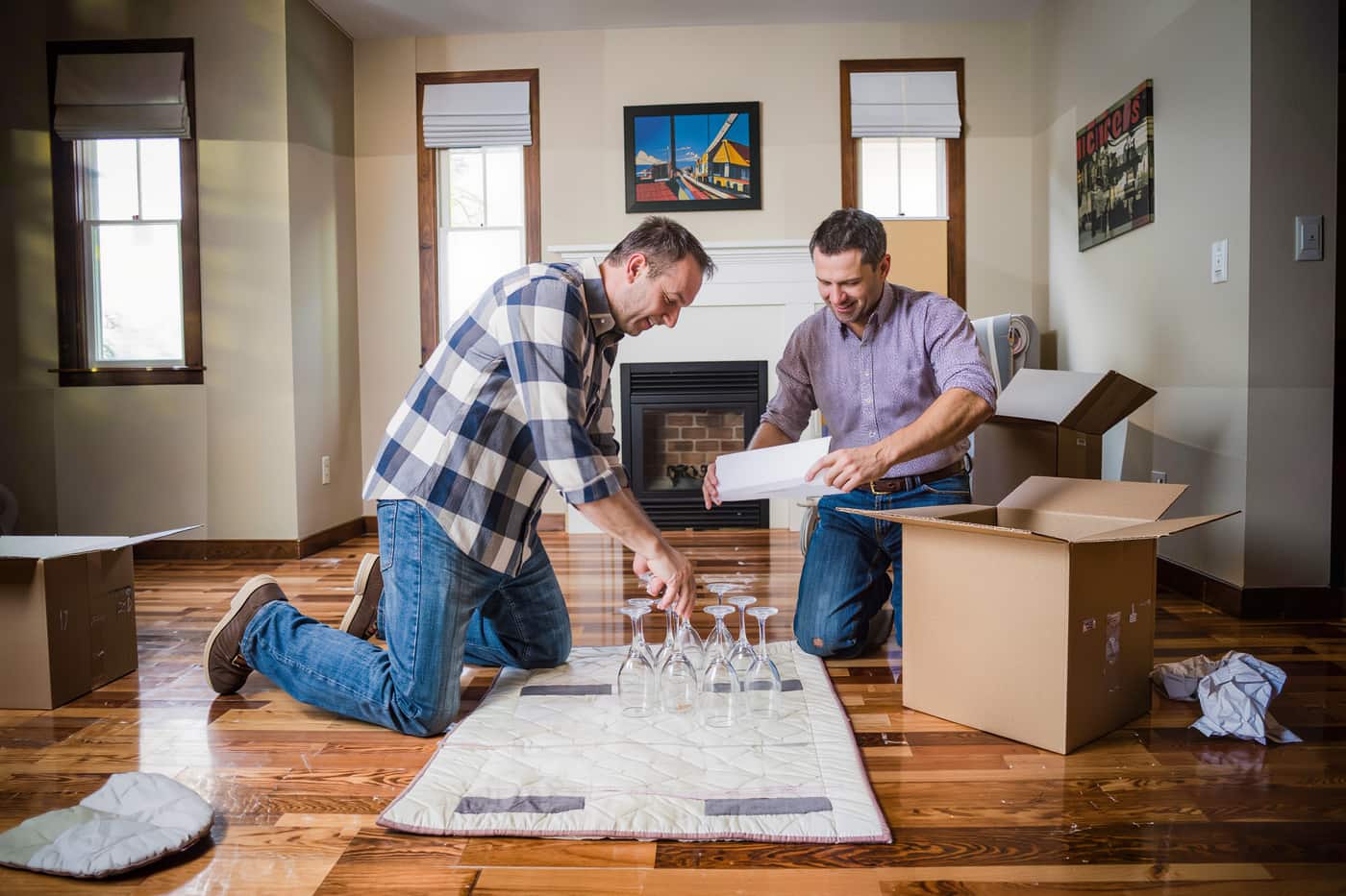 Two people kneeling on a living room floor unwrapping stemware from plain packing paper