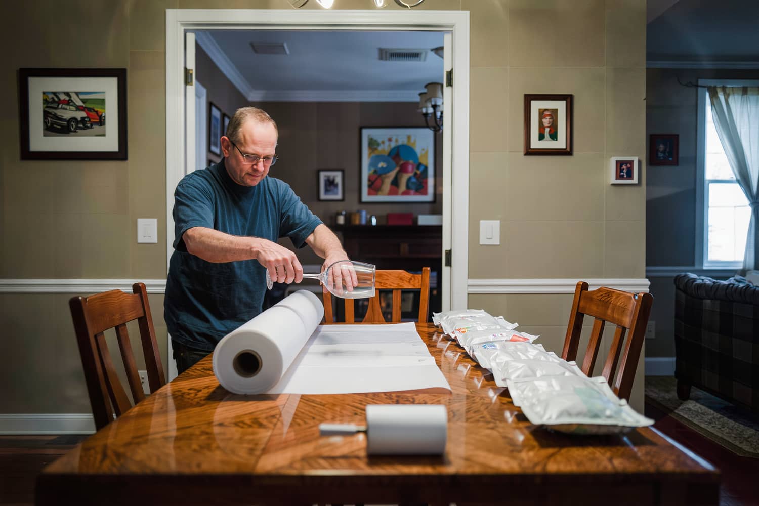 Hands rolling a stemmed glass into plain packing paper at a dining table packing station