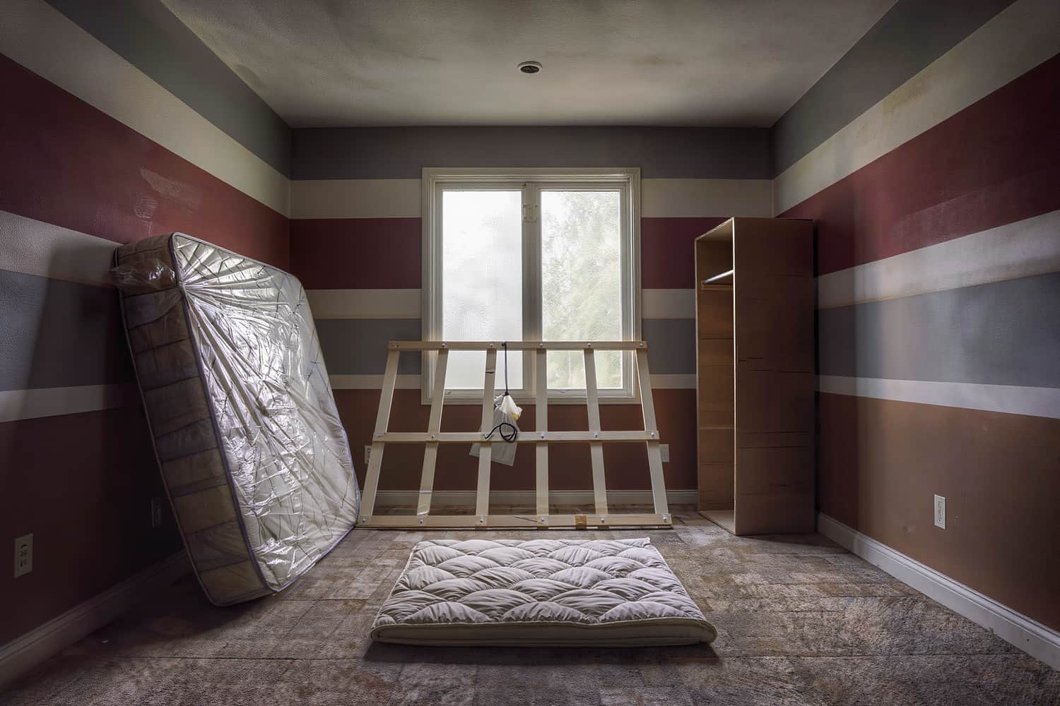 Stripped bedroom with a bagged mattress, banded bed rails and a wardrobe carton ready for the truck