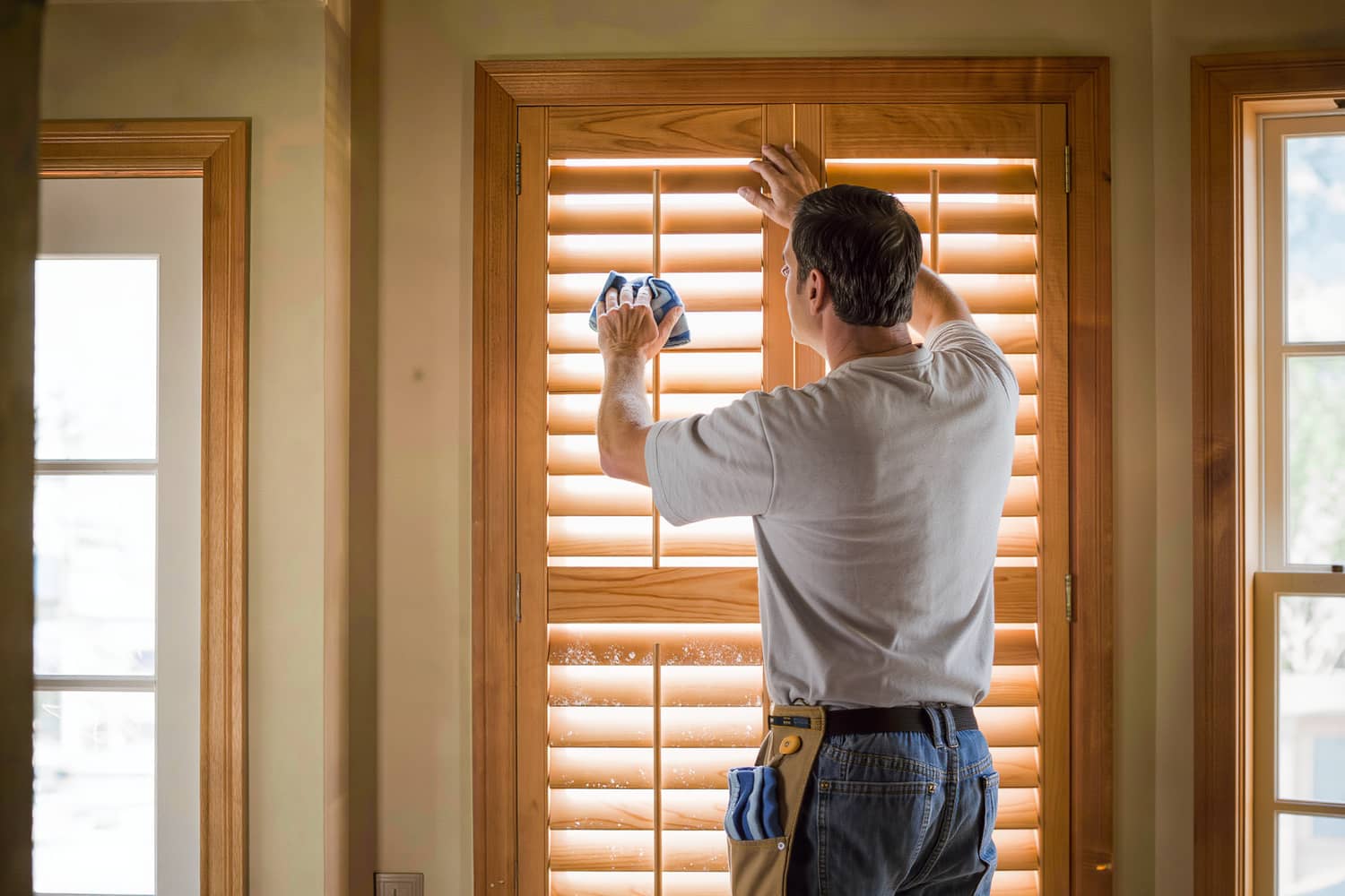 Cleaner detailing wooden shutter slats with a folded microfibre cloth