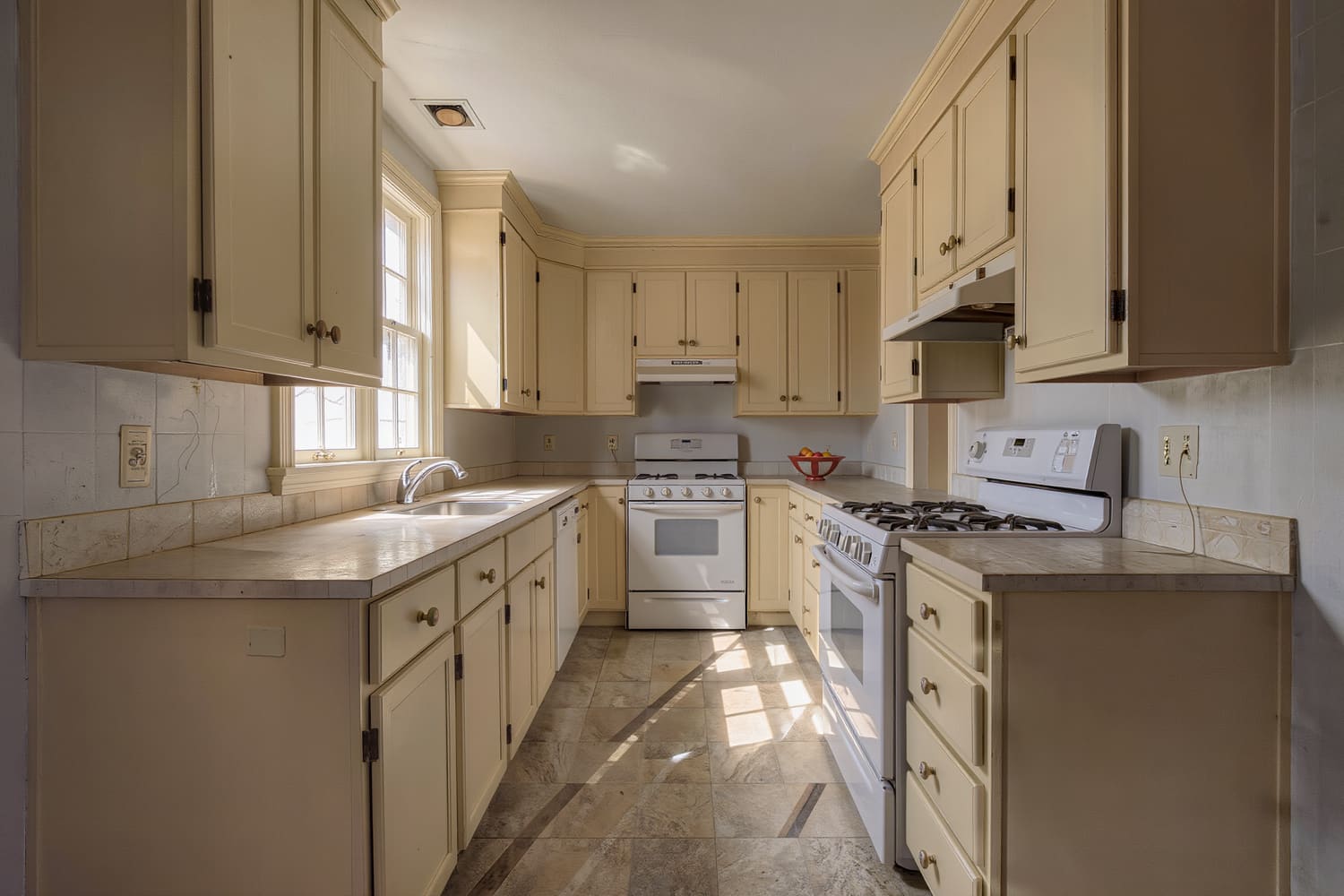 Galley kitchen with sunlight across the mopped floor and completely clear worktops