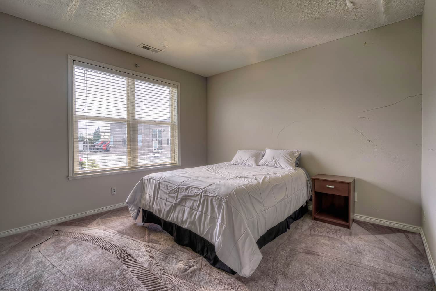 Made-up bedroom with crisp bedding, half-open blinds and fresh vacuum tracks by the bed