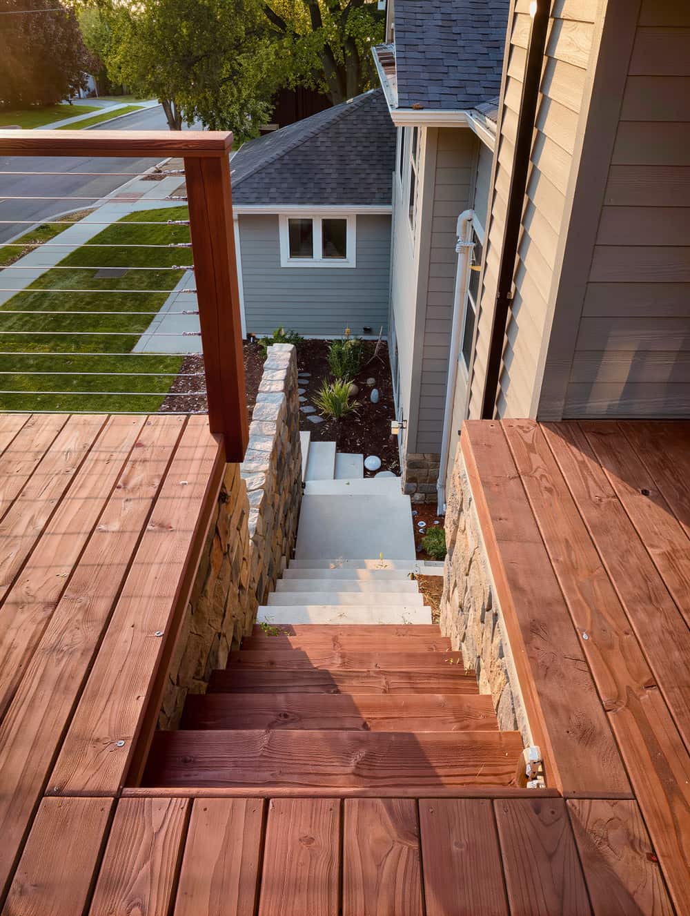 Redwood deck with cable railing looking down across three planted garden terraces