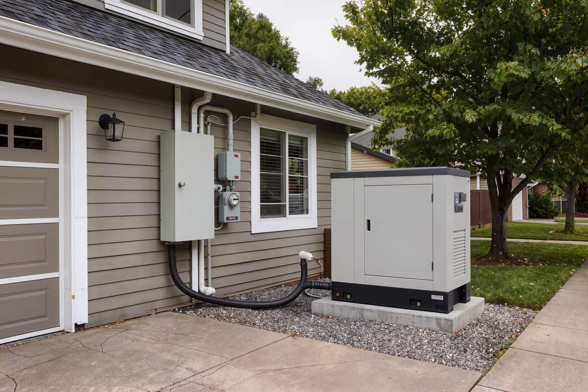 Transfer switch enclosure on lap siding beside a standby generator on a concrete pad