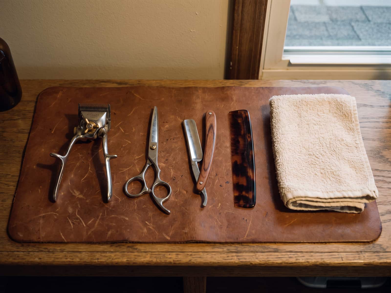 Clippers, shears, straight razor, comb and folded towel arranged on a leather mat