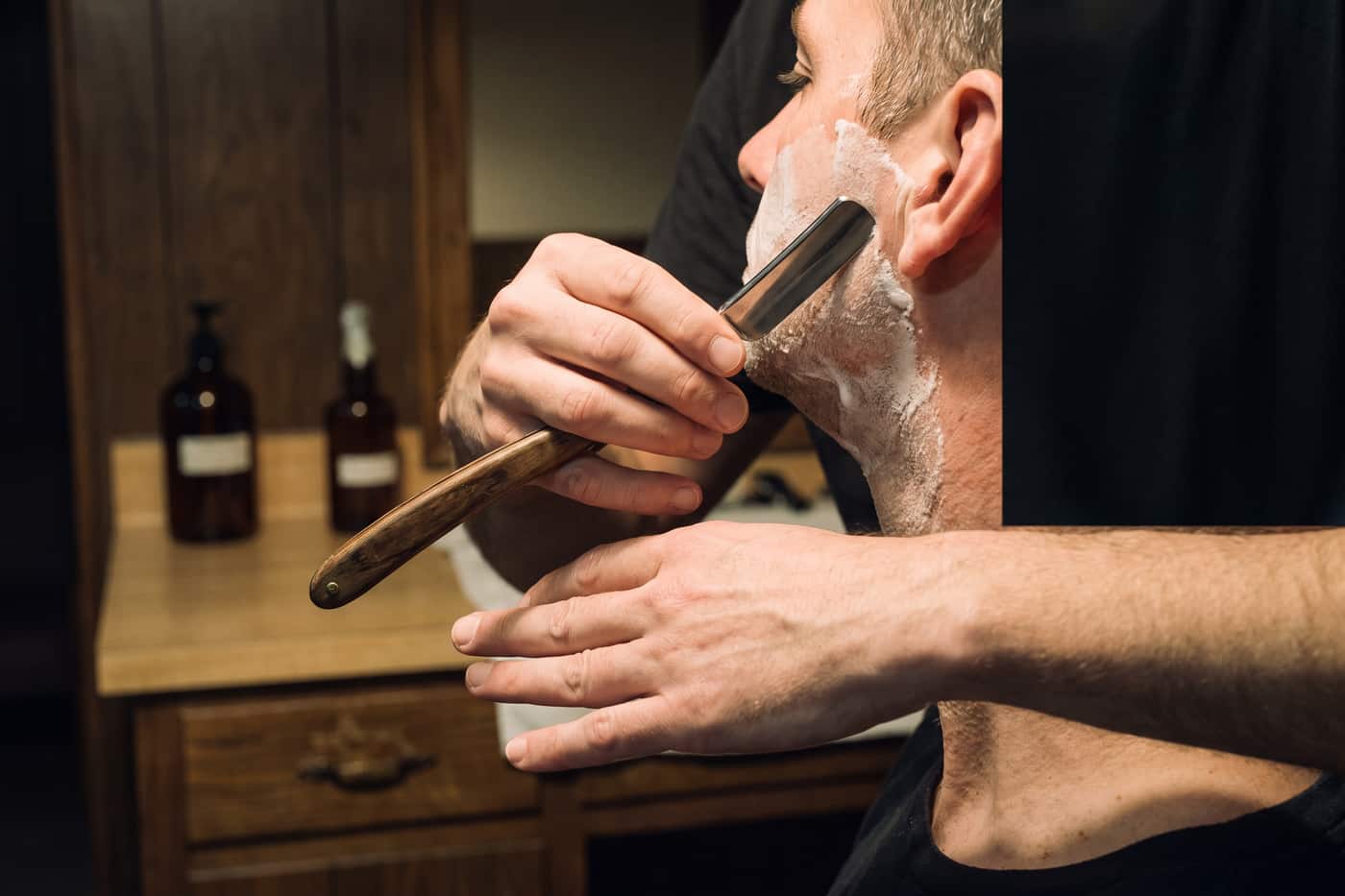 Straight razor drawn down a lathered cheek at a shallow angle