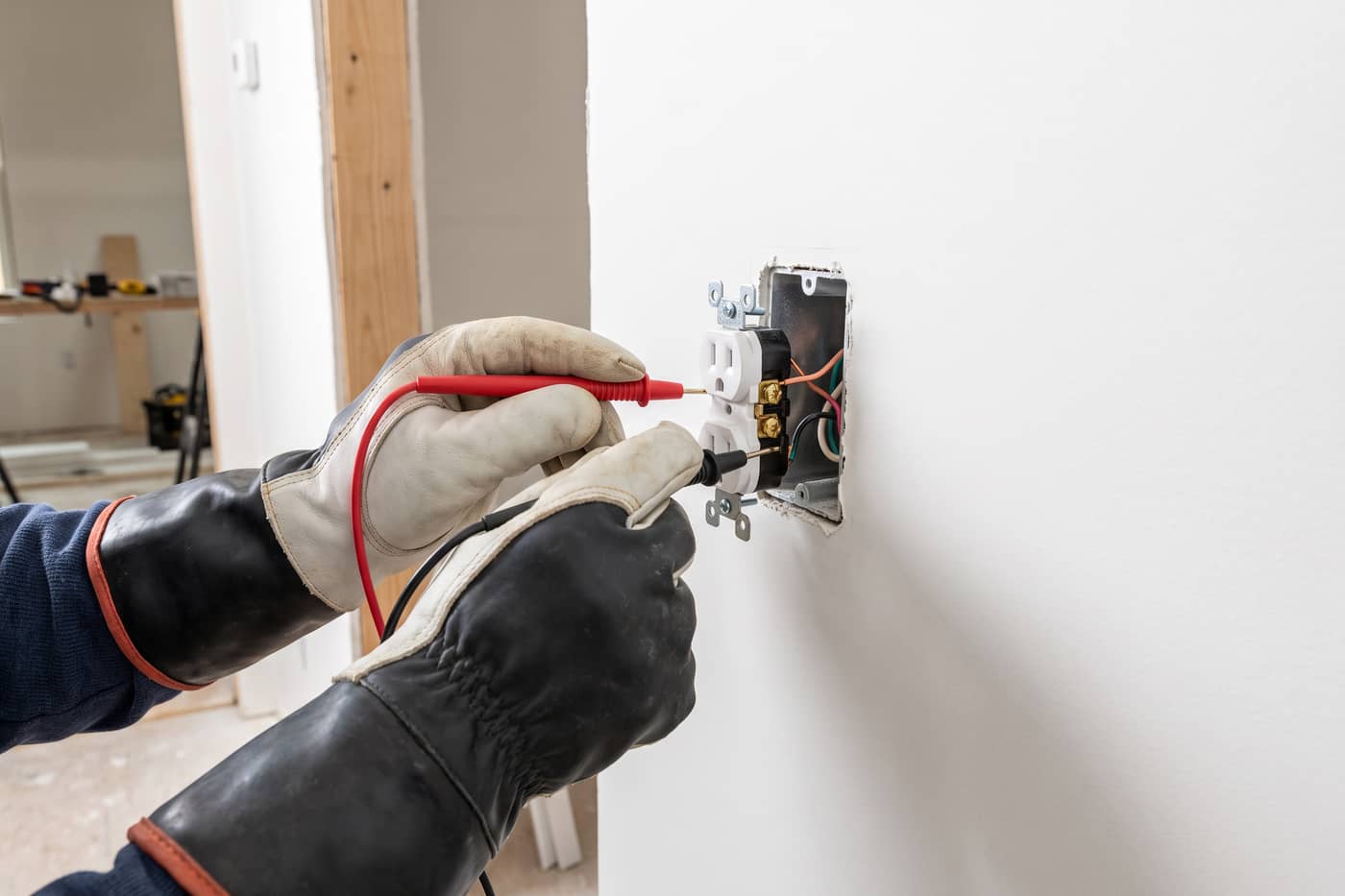 Multimeter probes held to a receptacle's terminals with the cover plate removed