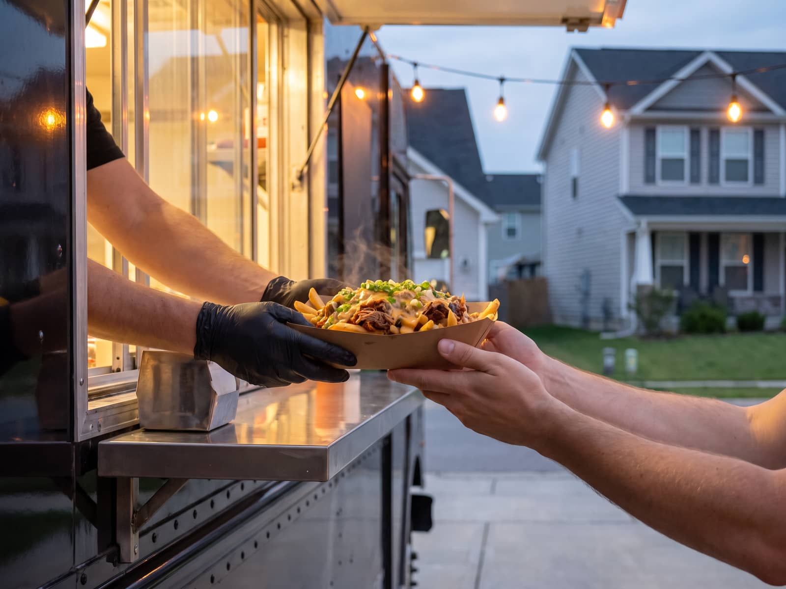 Food-truck service window at dusk, a hand passing a plain paper tray across the counter