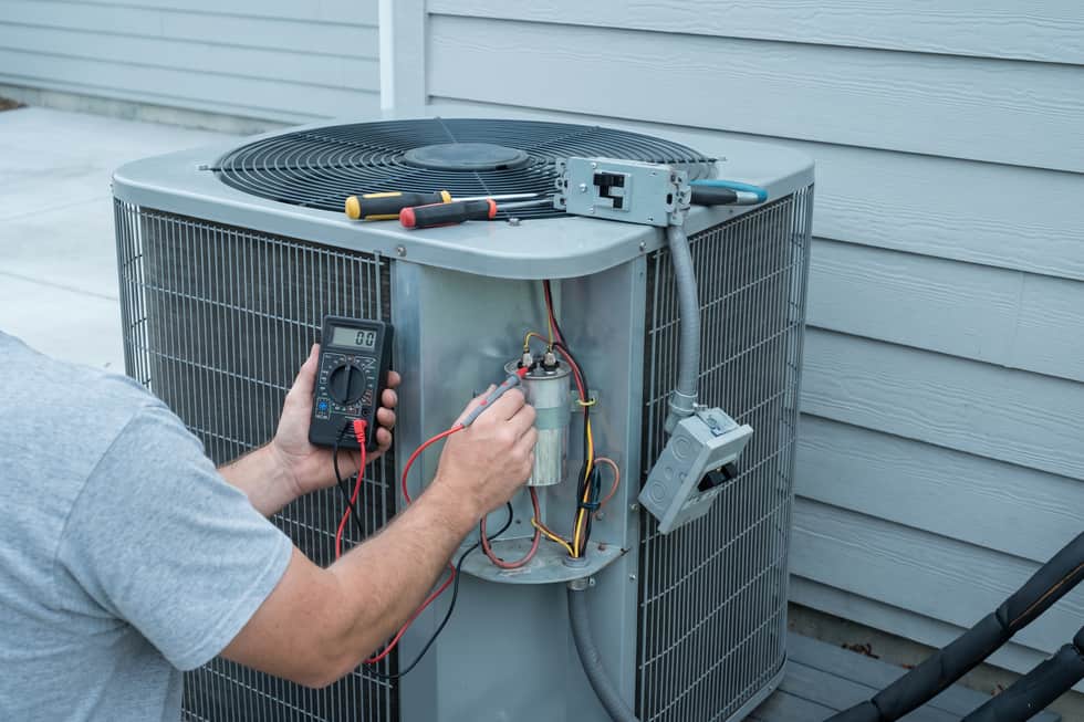Capacitor being tested with a multimeter on an open condenser panel, disconnect pulled