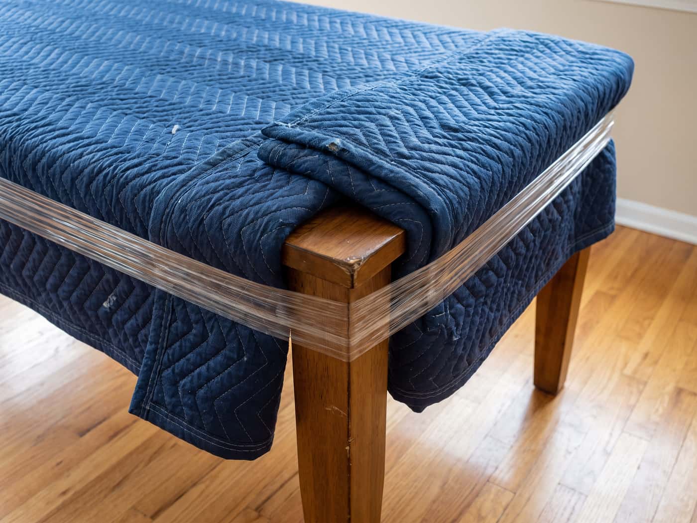 Close detail of a moving blanket drawn over a table corner and secured with a stretch-wrap band