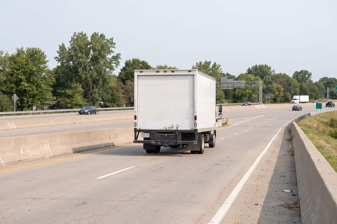 Loaded moving truck on an interstate, seen from behind in flat morning light
