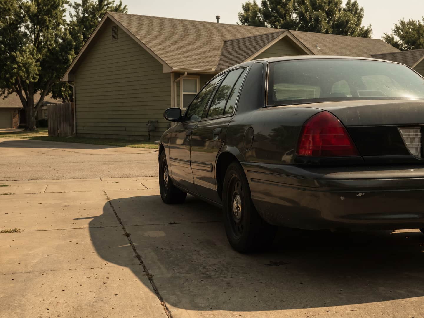 Dark sedan on a suburban driveway at golden hour with a long shadow across the concrete