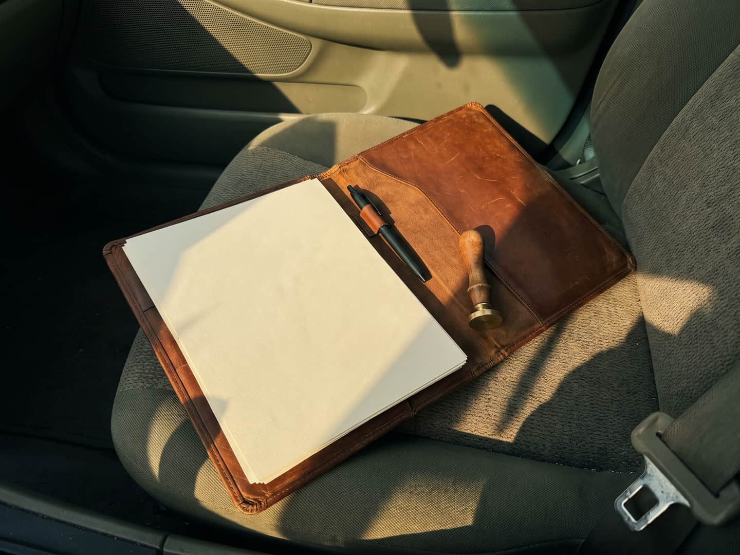 Open leather document folio on a car passenger seat with blank paper, a pen and a small hand seal