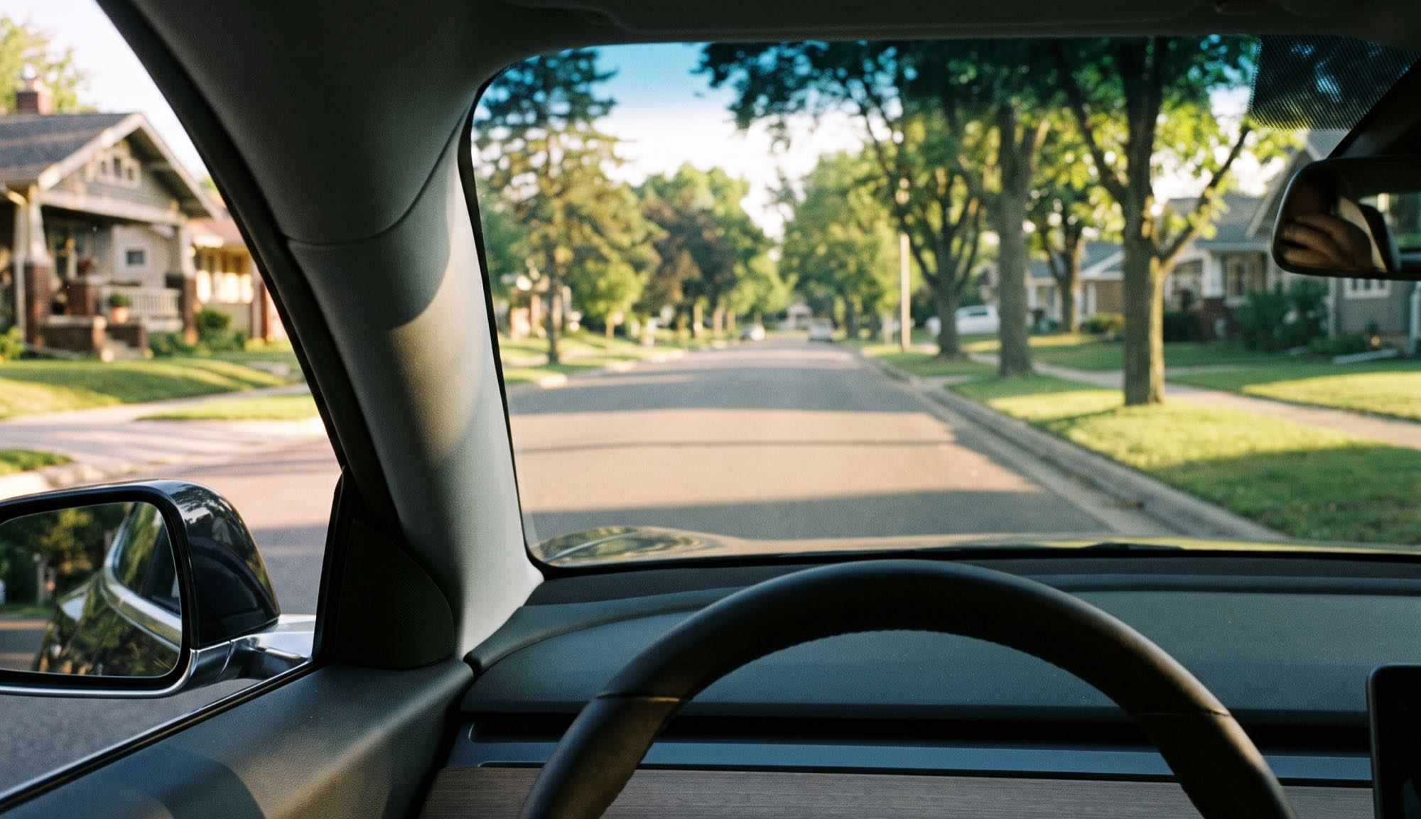 View through a car windshield down a quiet tree-lined suburban street at golden hour