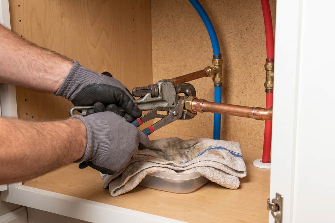 Wrench and channel locks on a copper union under a sink, towel and catch basin beneath