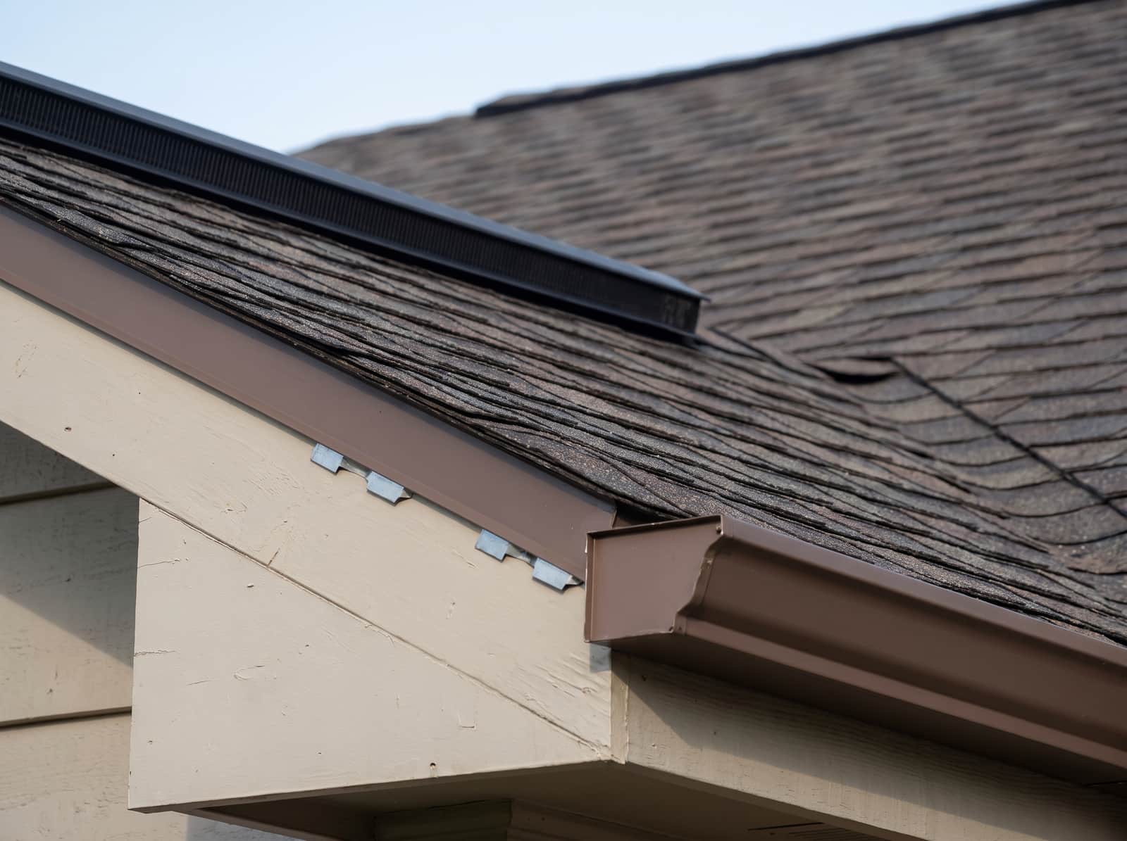 Close view of a finished roof edge where the rake meets the eave, showing the drip edge over the fascia and a gutter hung true