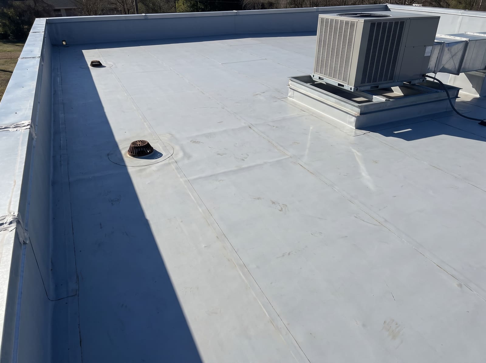 Flat single-ply membrane roof on a low commercial building, with roof drains and a curb-mounted rooftop unit