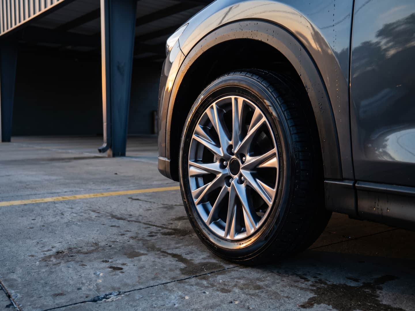 Cleaned alloy wheel and satin-dressed tire on the wash apron, water still beaded on the paint above the arch
